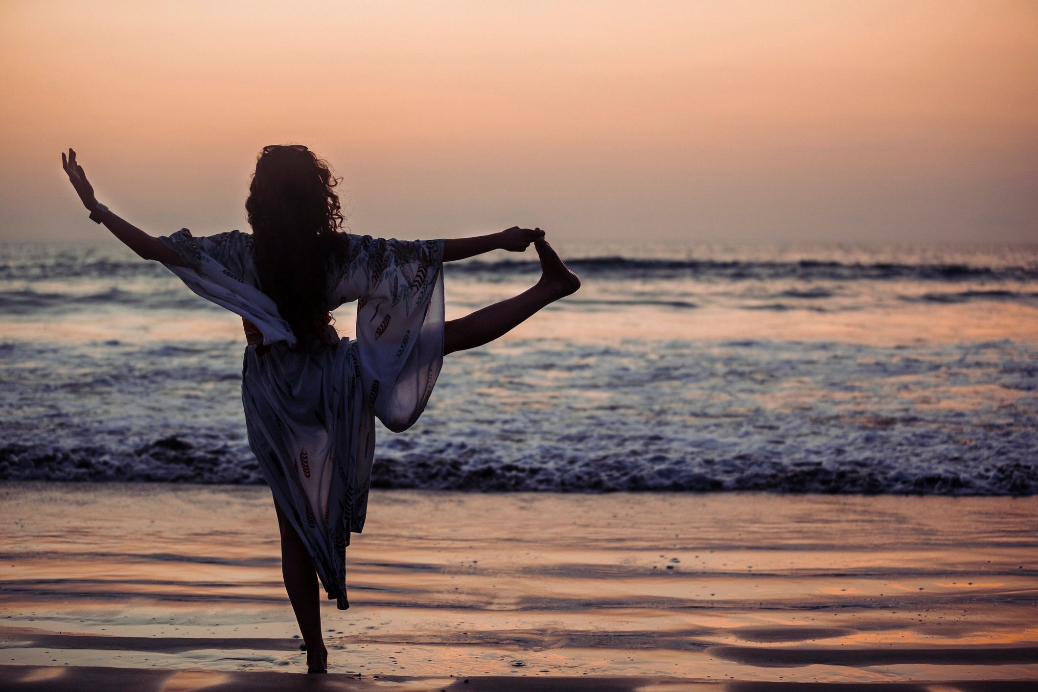 Woman standing on a beach at sunrise in a peaceful pose