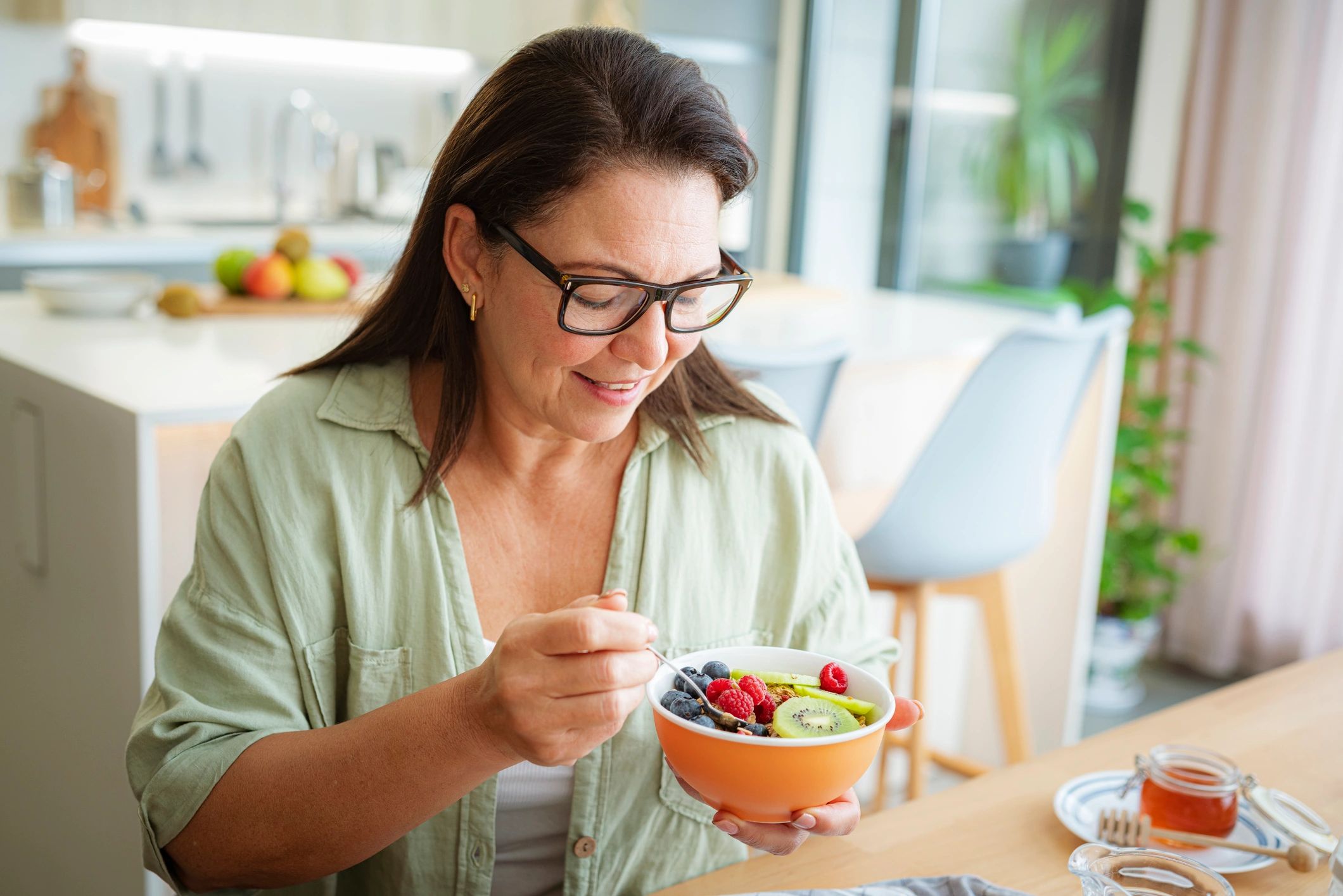Woman enjoying a nourishing bowl of fruit in a kitchen
